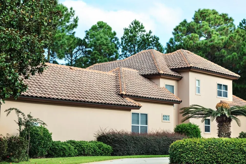 Tile roof above a stucco house surrounded by palms and other vegetation